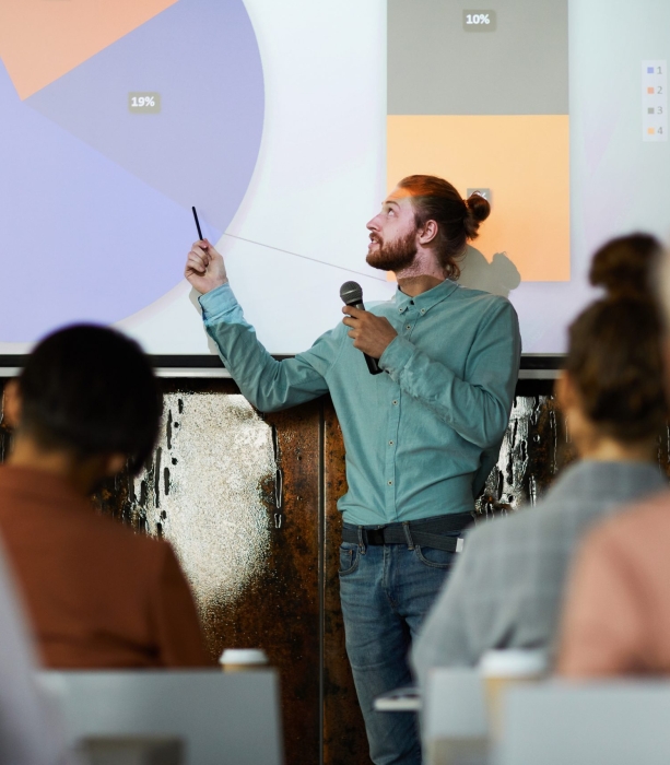 Portrait of contemporary bearded man giving presentation standing by projector screen in lecture hall, copy space